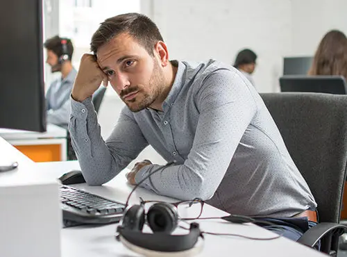 En mand sidder stresset og træt ved sin arbejdsplads på kontoret uden støjværn.